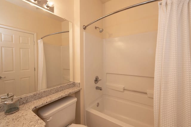 Bathroom with a toilet, granite countertop, and a bathtub with a shower curtain.