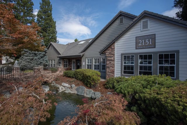 Sunset Summit Apartment Homes building exterior with stone accents, landscaping, and a small bridge over a water feature.