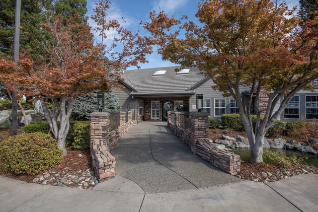 Exterior entrance to apartment complex with stone walls and autumn trees.