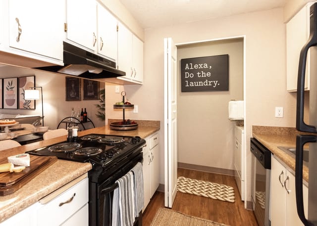Kitchen with black stove and cabinets, open doorway to laundry area with Alexa sign.
