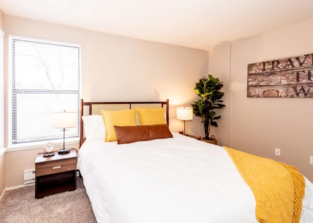 Bedroom with a queen-size bed, yellow accents, and a large window.