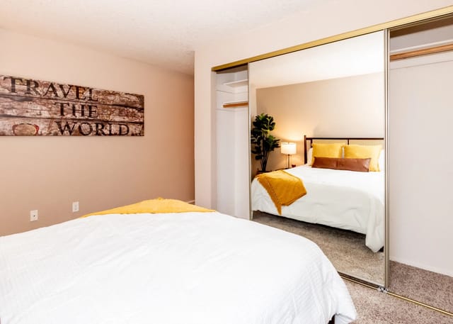 Bedroom with a queen-size bed, yellow pillows, and a mirrored closet door reflecting the bed.