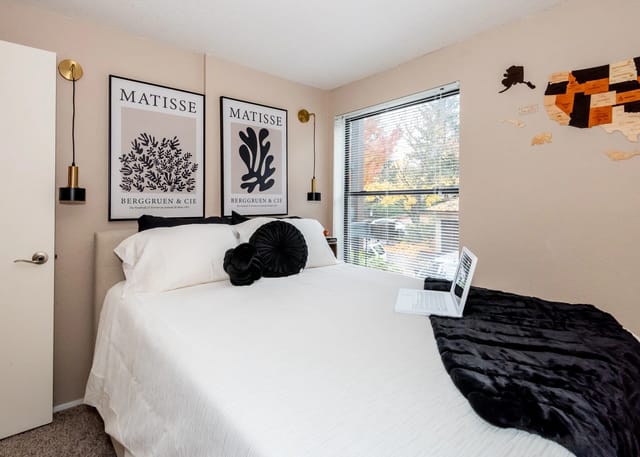 Bedroom with a queen-size bed, Matisse art prints, and a laptop on a black fur throw.