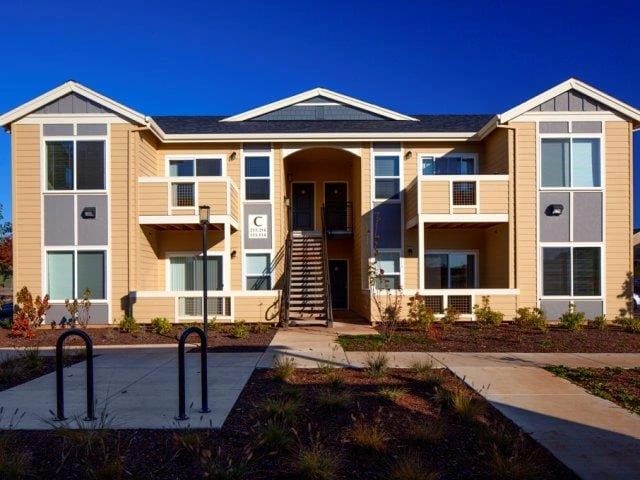 Exterior of a modern apartment building with tan siding and grey accents.