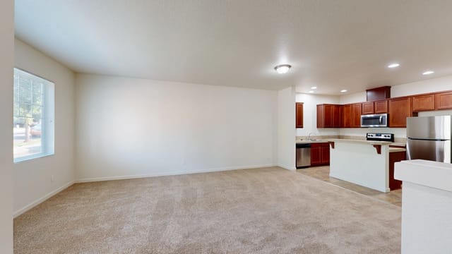 Spacious living room and kitchen area with carpet and wood cabinets.