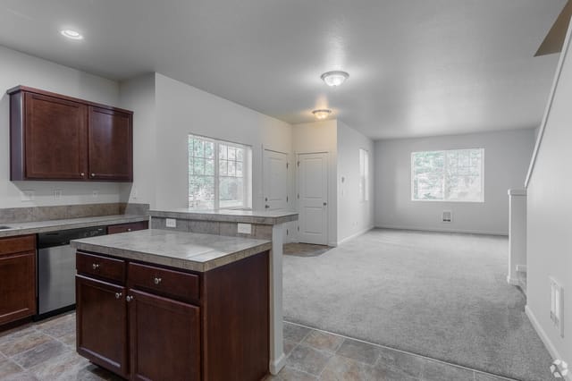 Kitchen and living room area with dark wood cabinets, granite countertops, and carpeted floor.