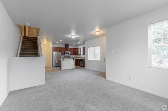 Spacious living room with carpet and stairs leading to the second floor.