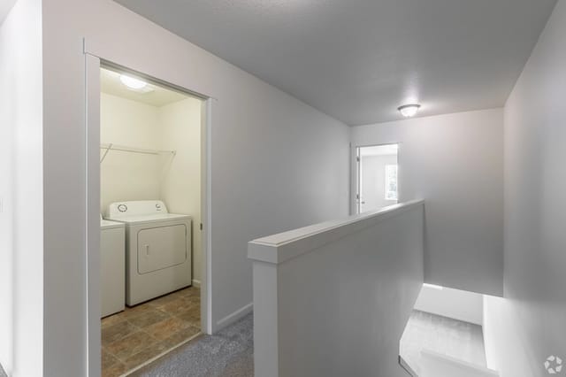 Laundry closet with washer and dryer on hallway leading to stairs.