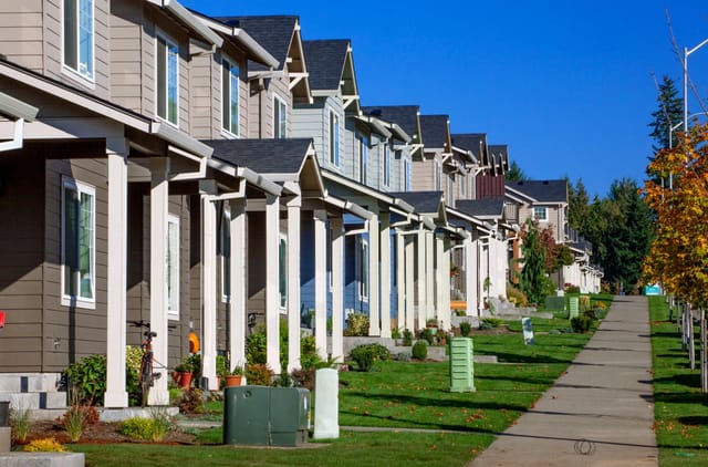 Row of townhomes with covered porches and white columns, a sidewalk leading away on a sunny day.