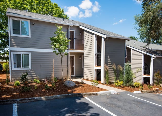 Exterior view of apartment buildings with a parking lot in the foreground.