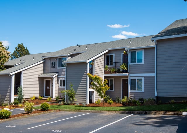 Exterior view of apartment buildings with parking lot in foreground.
