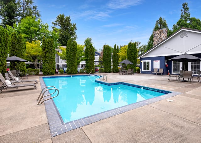 Outdoor swimming pool with lounge chairs and umbrellas, next to a building with outdoor seating.