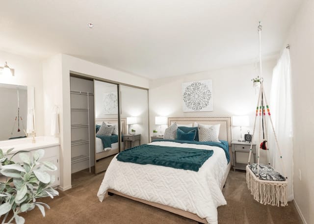 Bedroom with a queen-size bed, mirrored closet doors, and a boho-style macrame hanging chair.