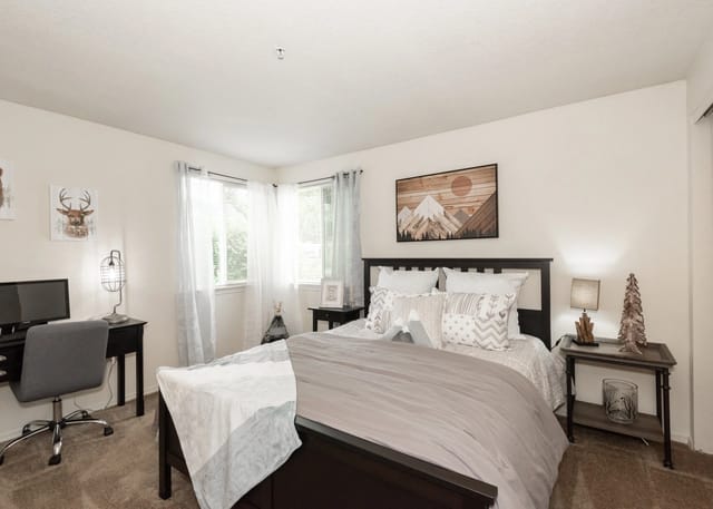 A well-decorated bedroom with a queen-size bed, desk, and large windows.