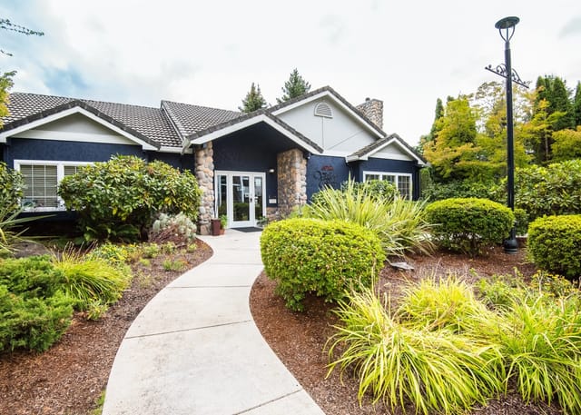 Walkway leading to the entrance of a navy blue building with stone accents and landscaping.
