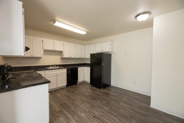 Kitchen with white cabinets, black countertops, refrigerator, and stove.