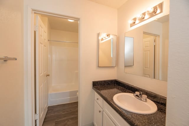 Bathroom with vanity, sink, mirror, and bathtub/shower combo visible through doorway.