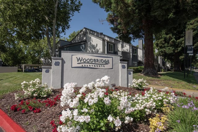 Woodbridge Apartments monument sign with blooming flowers in the foreground.