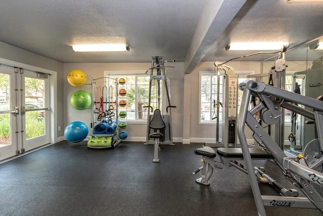 Interior of a well-equipped apartment complex gym with various weight machines, exercise balls, and resistance bands.
