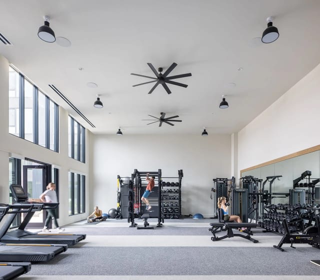 Bright gym in a multifamily building with treadmills, weights, and large windows.