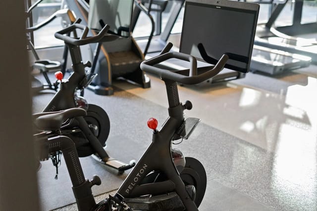 Indoor building gym featuring Peloton stationary bikes with screens.