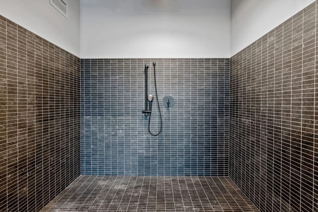 Shower stall with dark gray tile walls and handheld shower.