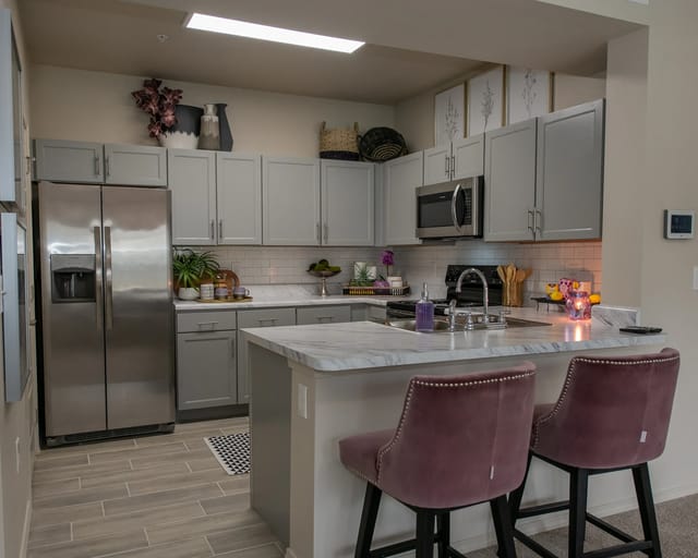 A kitchen with a marble countertop and two burgundy barstools.