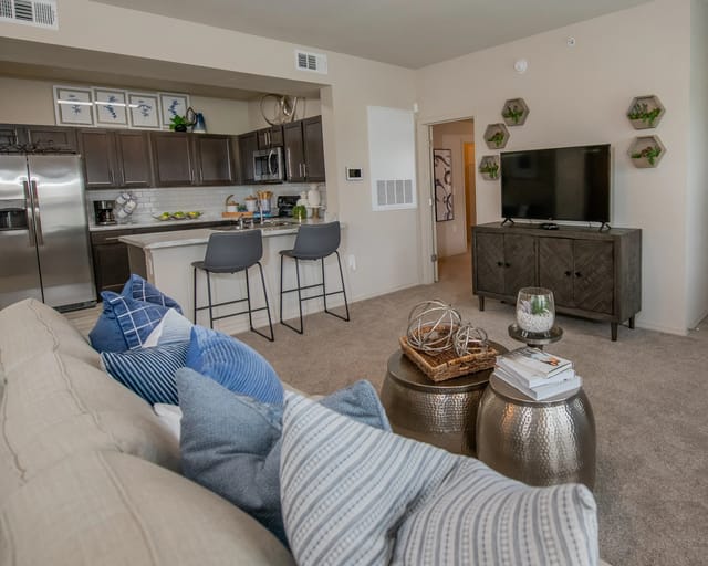 A living room with a couch, a coffee table, and a kitchen area in the background.