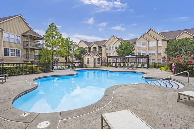 Outdoor swimming pool with lounge chairs and apartment buildings in the background.