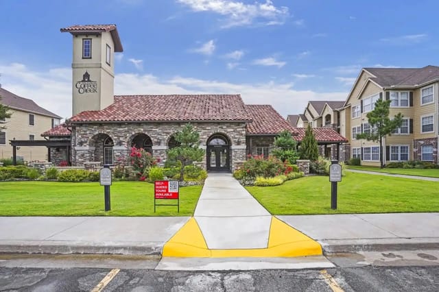 Exterior view of a stone-clad clubhouse with a red-tile roof and landscaped entrance at an apartment community.