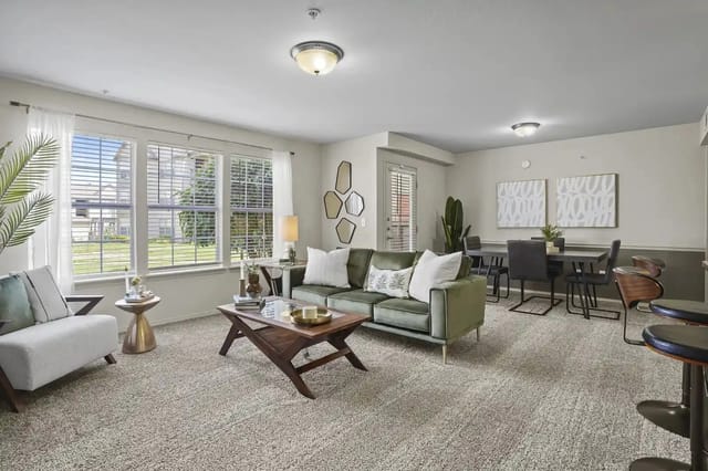 Living room in a model apartment with large windows, a green sofa, and a dining area.