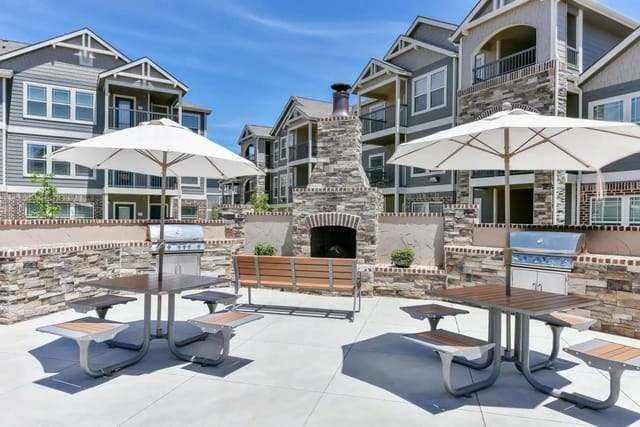 Outdoor community courtyard with a stone fireplace, grills, benches, and umbrellas.