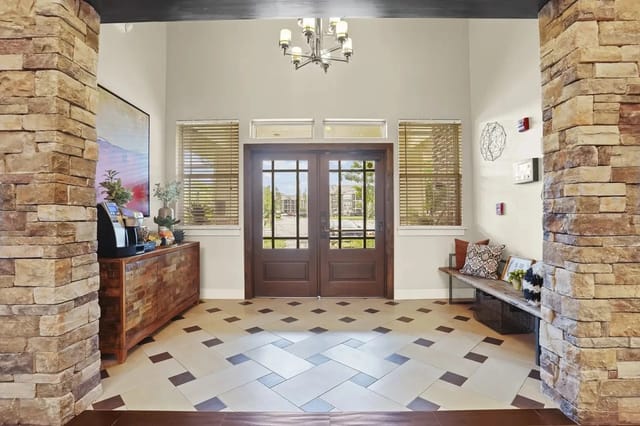 Lobby area with double wooden doors, stone columns, and a patterned tile floor.