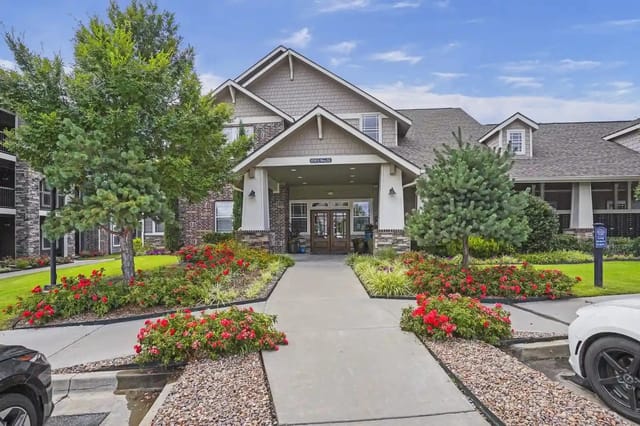 Exterior entrance of an apartment community with a covered drop-off and landscaped flower beds.
