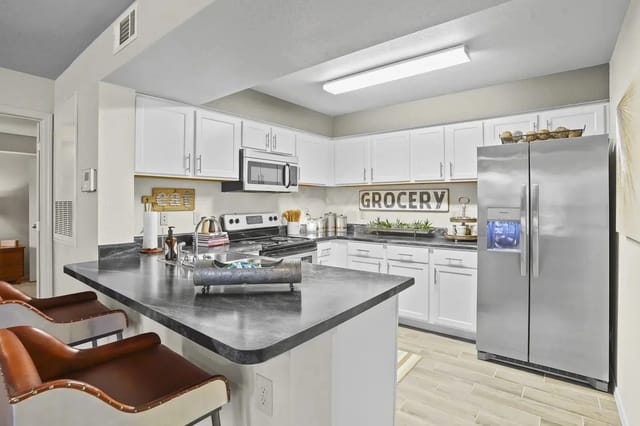 Bright apartment kitchen with white cabinets, stainless steel refrigerator, and an island.