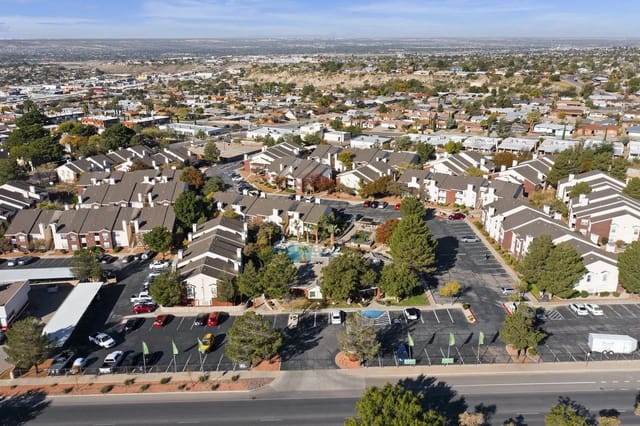 Aerial view of a large apartment complex with multiple beige buildings, parking lots, and trees.