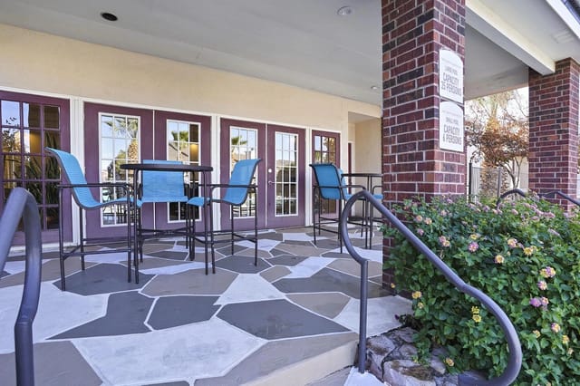 Outdoor seating area at an apartment building entrance with purple-framed glass doors and blue chairs.