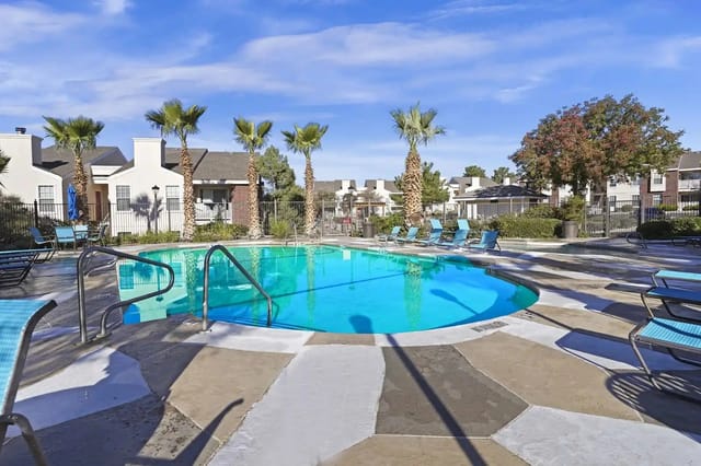 Outdoor apartment community pool with blue lounge chairs and palm trees.