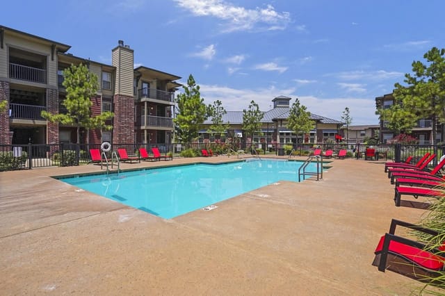 Outdoor swimming pool with lounge chairs and apartment buildings in the background.