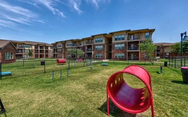 Fenced grassy courtyard with playground between apartment buildings.