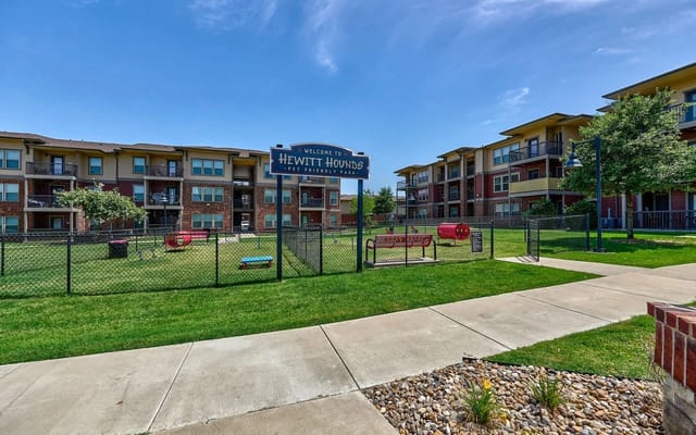 Exterior view of a fenced pet park within an apartment community, with buildings in the background.