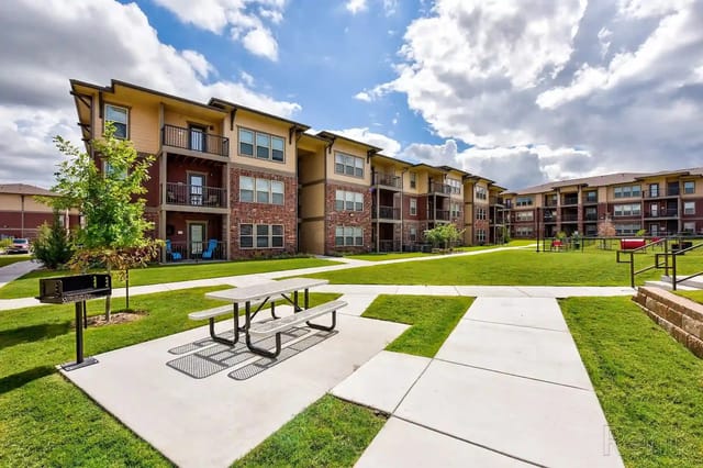 Exterior view of a multi-building apartment community with green lawns and a picnic area.