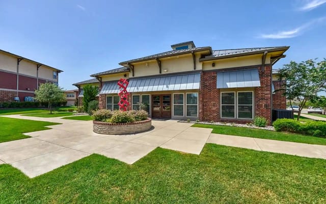 Exterior view of a brick multifamily building with glass doors, windows, and a landscaped entrance.