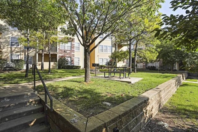 Outdoor communal courtyard with trees, grass, and a picnic table near apartment buildings.