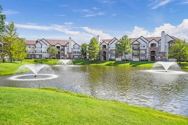 Exterior view of a multi-building apartment complex with a pond and fountains.