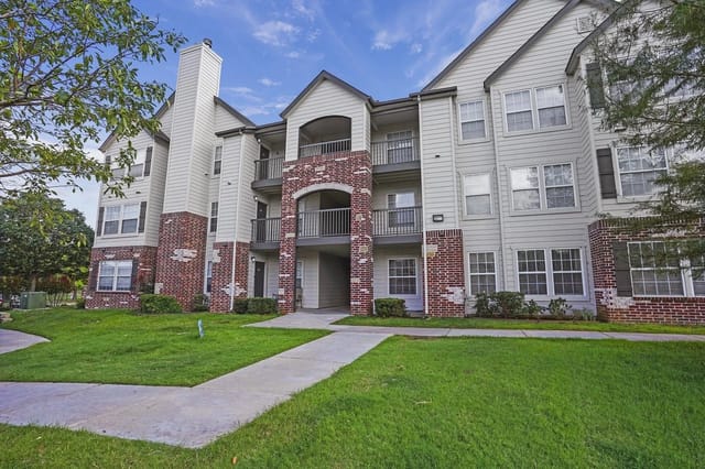 Exterior view of a multi-family apartment building with brick accents and green lawn.