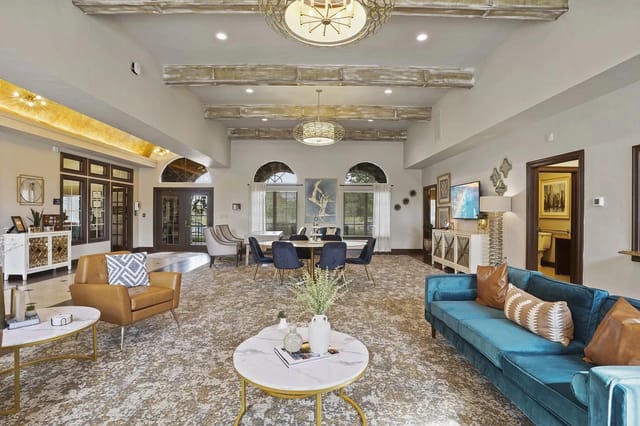 Interior of a spacious apartment community lounge with seating, tables, and decorative lighting.