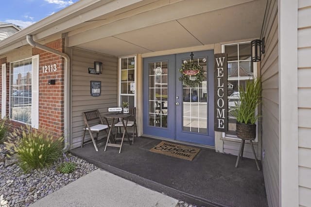 Front entrance of an apartment building with blue double doors, a welcome sign, and a small seating area.