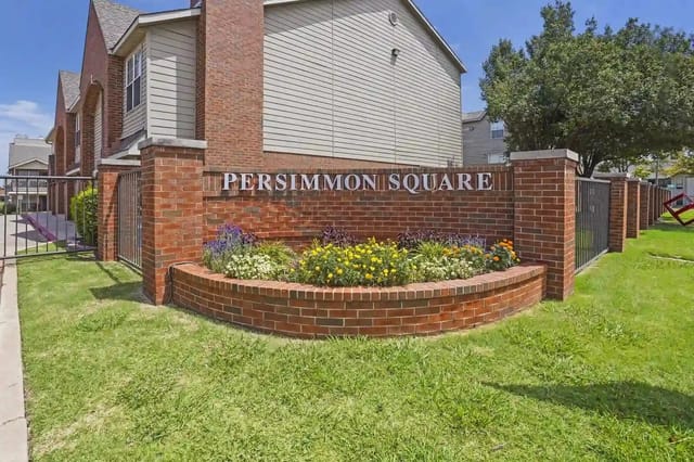 Brick sign wall with 'PERSIMMON SQUARE' and surrounding flower beds at the property entrance.