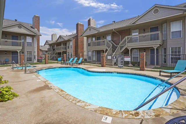 Outdoor community pool at an apartment complex with lounge chairs and surrounding buildings.
